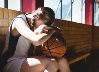 Une jeune basketteuse assise, la tête dans les bras, serre son ballon